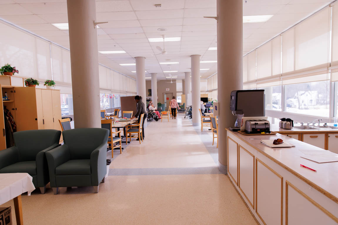 facility common area for activities with tables, chairs, a kitchen, and bright windows